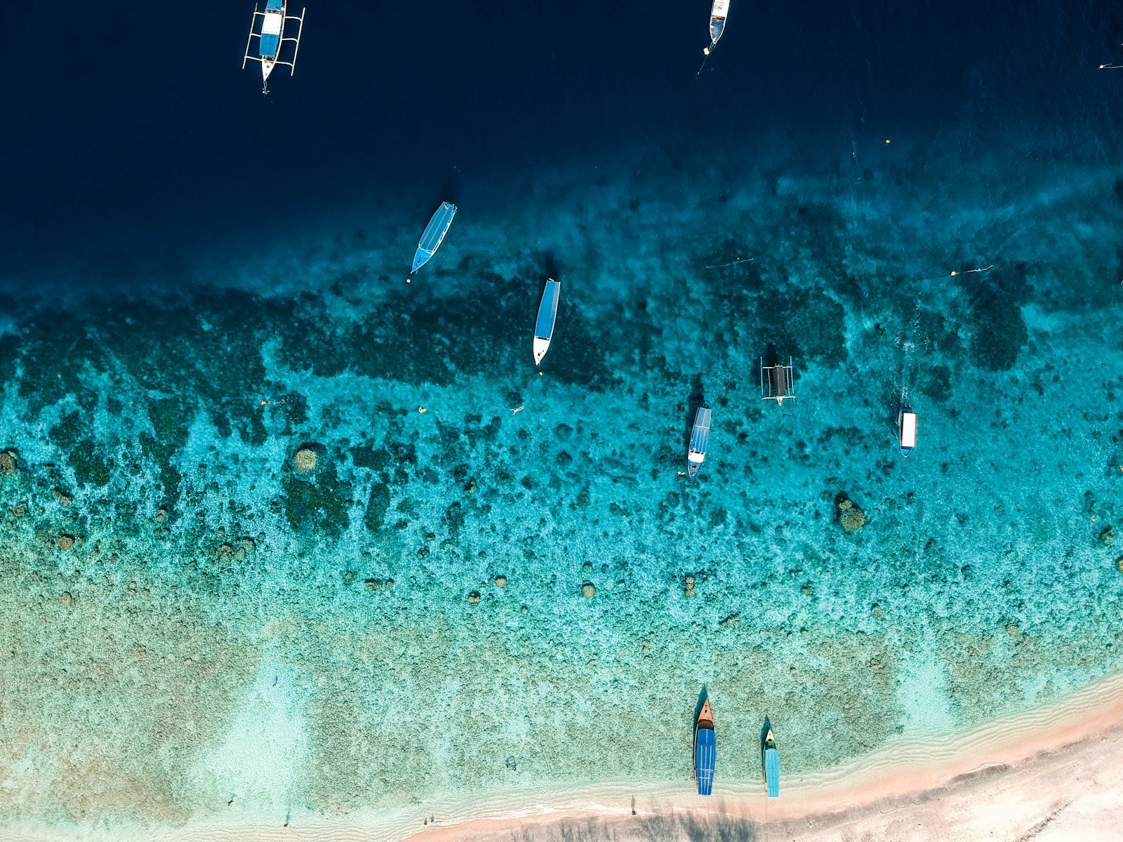 Boats float on clear turquoise water and sand.